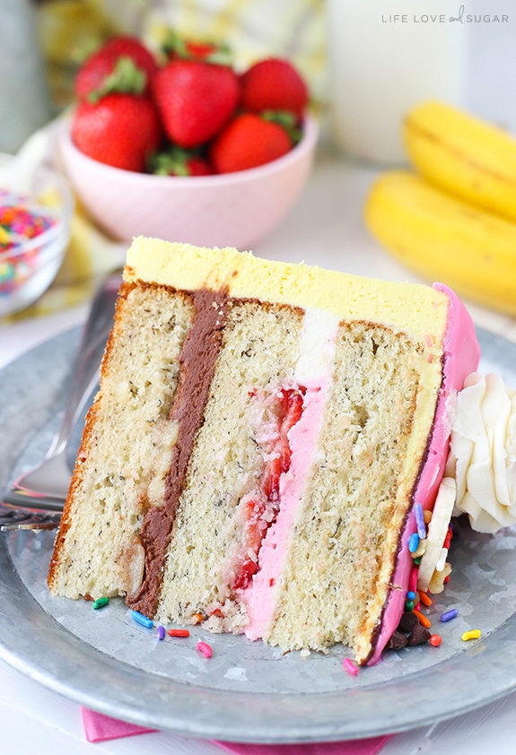 Banana Split Layer Cake - layers of moist banana cake with chocolate and strawberry buttercream filling, sliced bananas and strawberries, nuts, sprinkles and chocolate ganache! Banana split cake heaven!