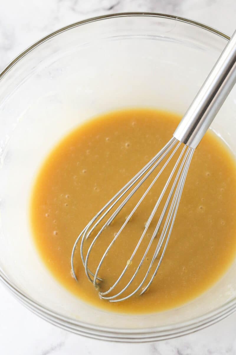 A whisk in a bowl with melted butter, oil, sugar, and vanilla
