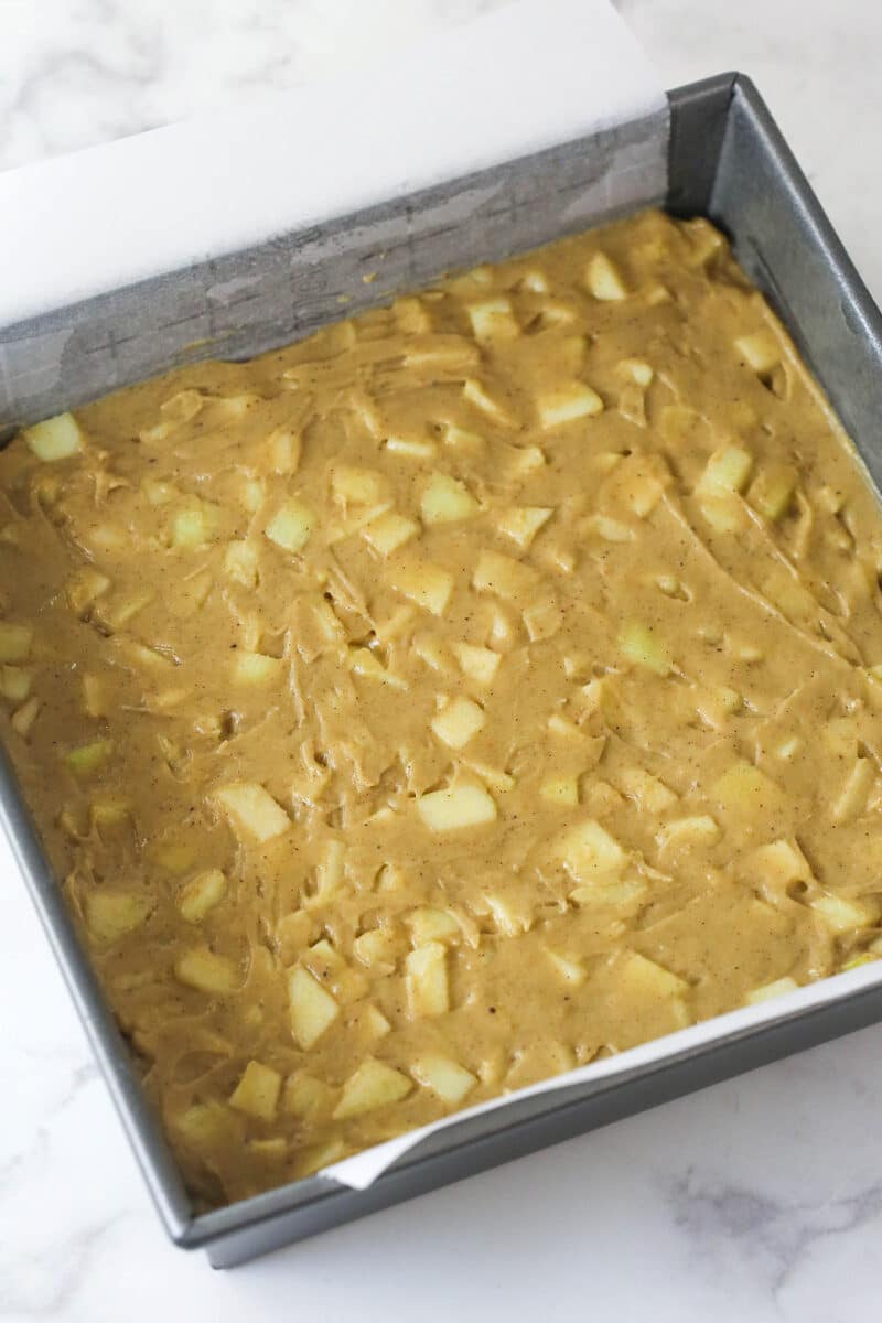 Every bite of these apple streusel bars is dotted with crunchy apples and warm fall flavors. Easy to make & perfect for breakfast or dessert! Apple bar batter in a square pan