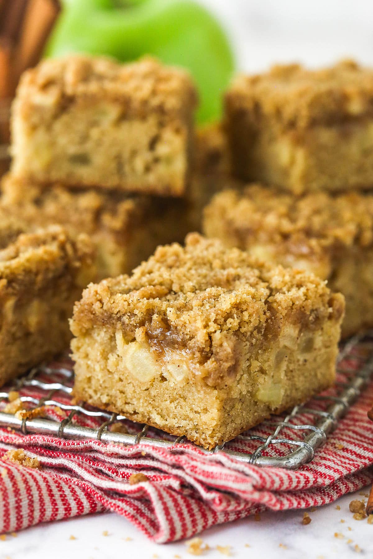 Every bite of these apple streusel bars is dotted with crunchy apples and warm fall flavors. Easy to make & perfect for breakfast or dessert! Close up of apple streusel bars stacked on a cooling rack
