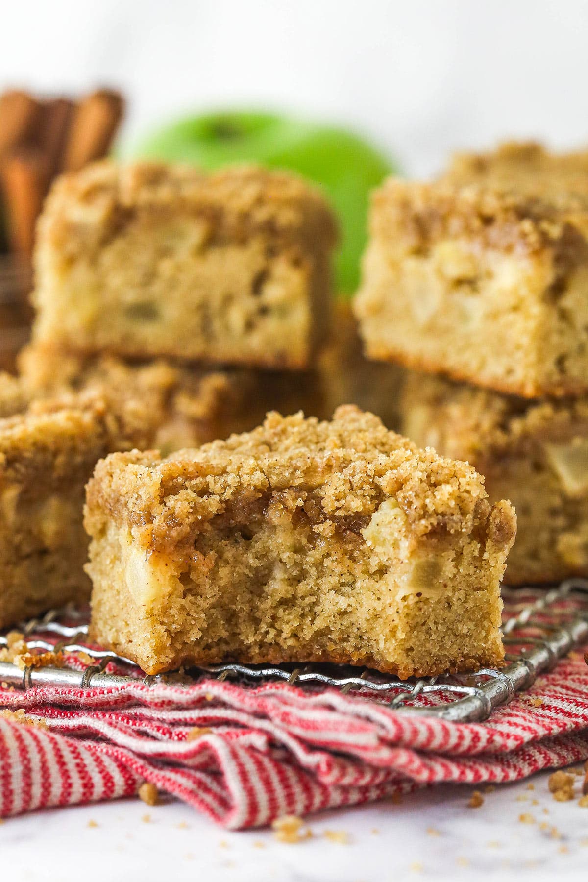 Every bite of these apple streusel bars is dotted with crunchy apples and warm fall flavors. Easy to make & perfect for breakfast or dessert! Apple streusel bars stacked on a wire rack, one with a bite missing