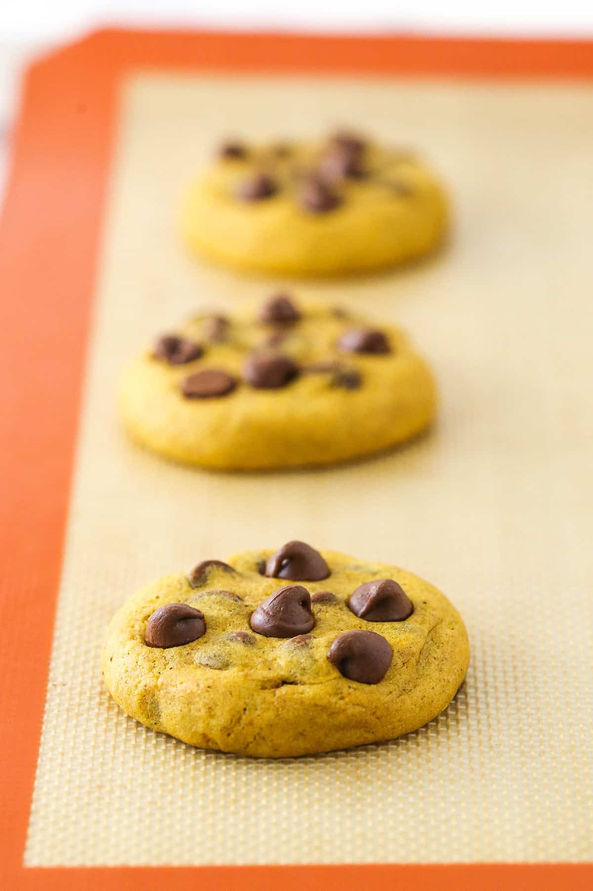 Three baked cookies on a baking sheet and baking mat.