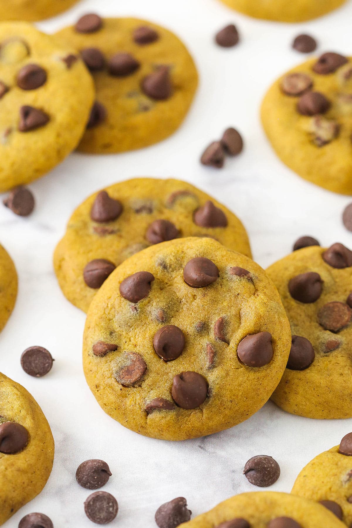 Pumpkin chocolate chip cookies scattered around on marble countertop.