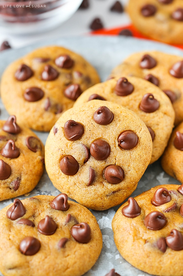 Pumpkin Chocolate Chip Cookies Piled Up on a Plate with a Bowl of Chocolate Chips in the Background