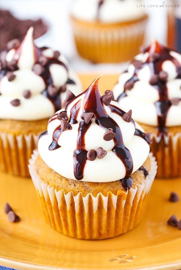 A Pumpkin Cupcake topped with cream cheese frosting, chocolate chips, and chocolate drizzle.