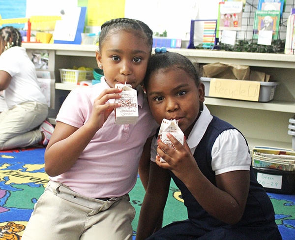 Two Girls Sipping From Their Milk Cartons Through Straws