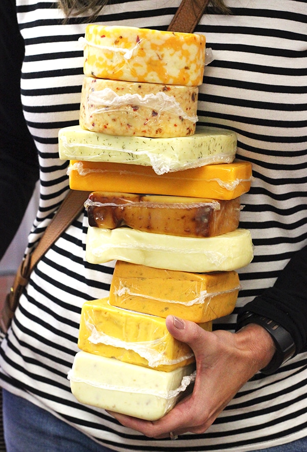 A Woman in a Black and White Striped Shirt Holding a Stack of Cheeses