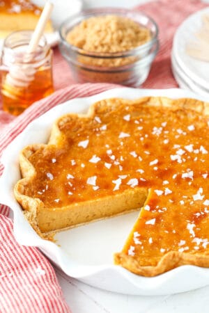 A homemade honey pie in a white pie plate with one slice missing