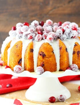 A cranberry bundt cake with white chocolate ganache on top of a cake stand
