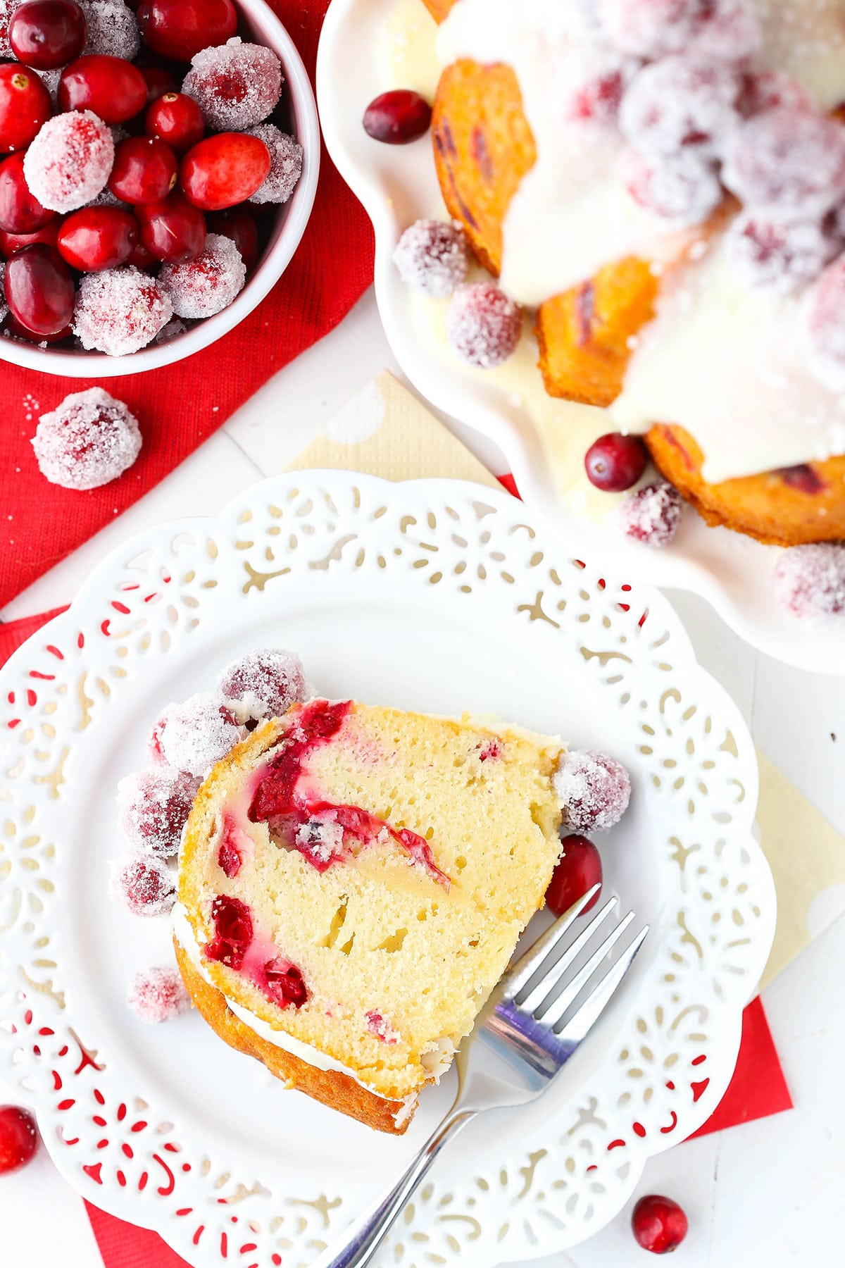 A piece of cranberry white chocolate bundt cake on a plate with a bowl of cranberries beside it