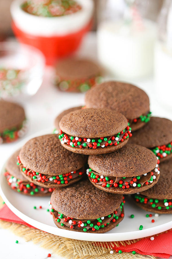 A bunch of Chocolate Cookie Sandwiches with sprinkles stacked on a white plate