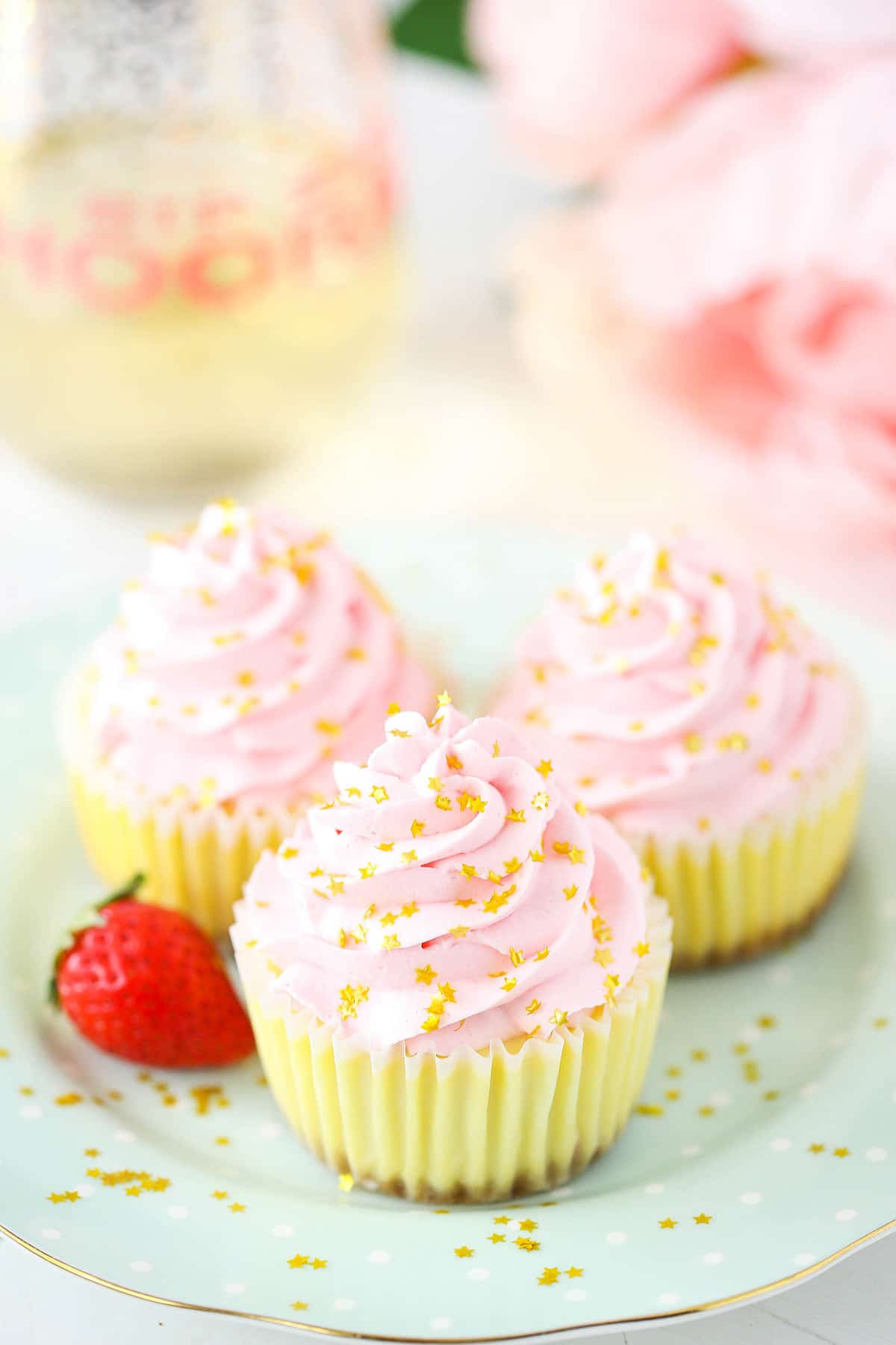 Three champagne cheesecake bites on a plate with a fresh strawberry