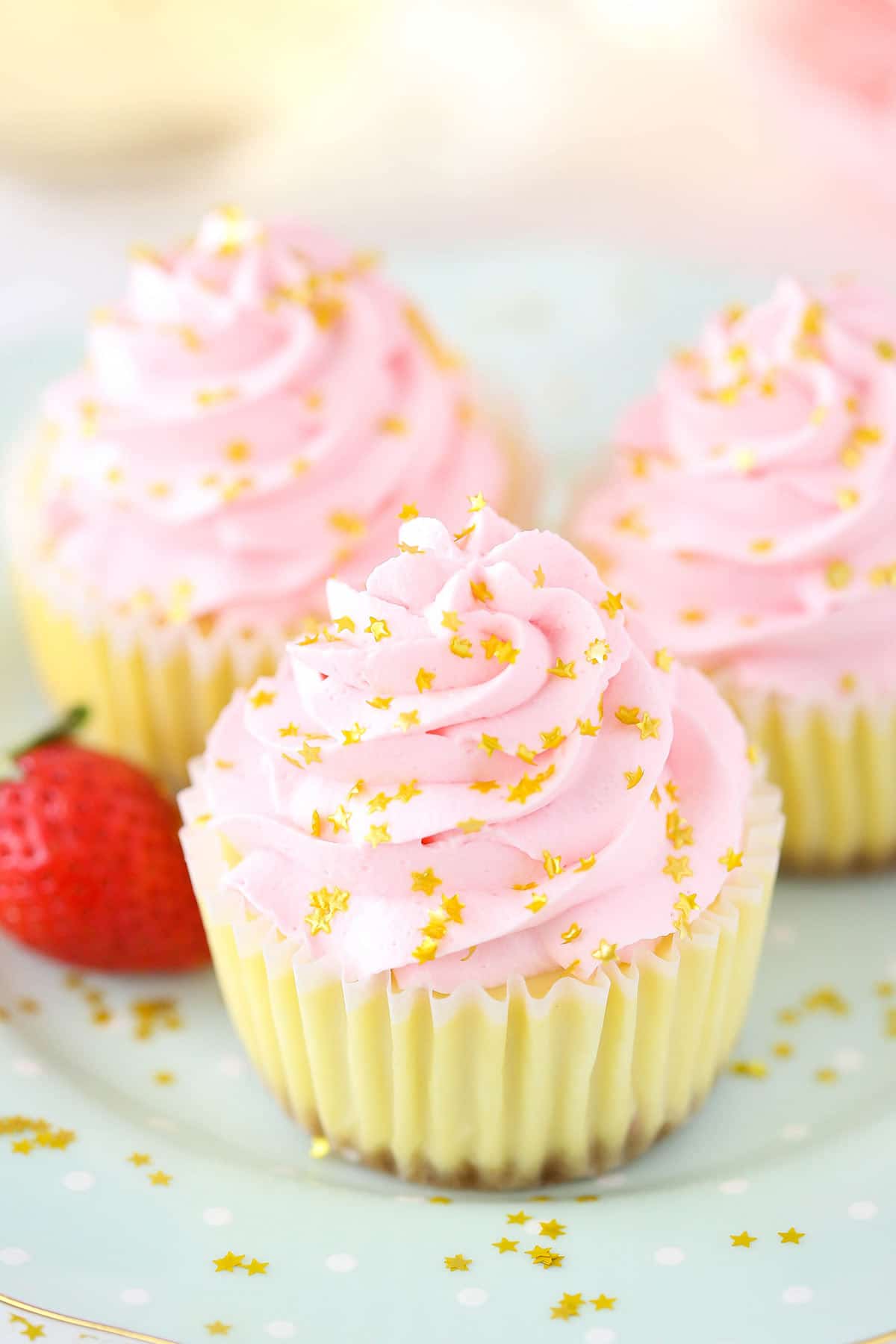 A close-up shot of three strawberry champagne cheesecake cupcakes on top of a polka dotted plate