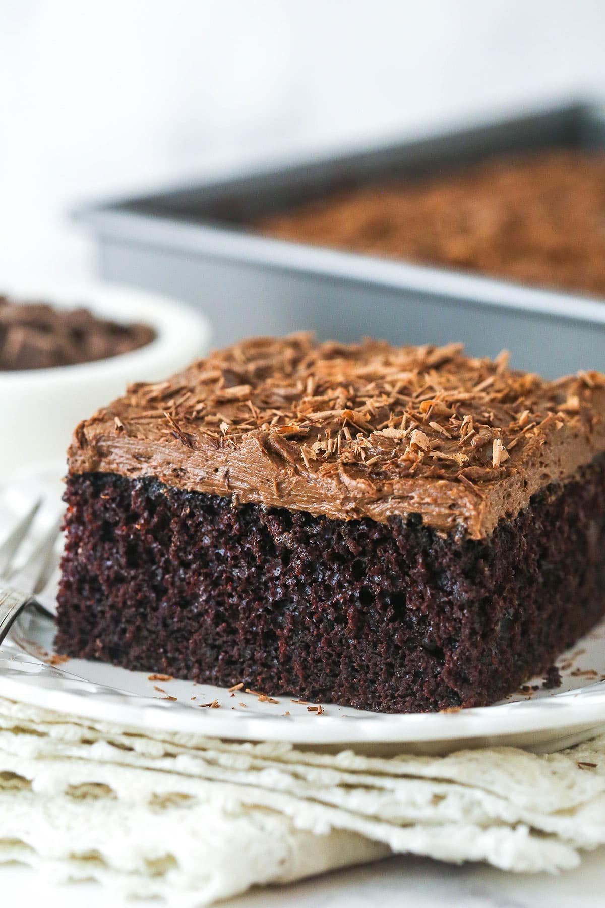 This fast-baking chocolate sheet cake is so moist and flavorful and the chocolate buttercream on top is light, fluffy, and totally to die for. close up of a slice of chocolate sheet cake on white plate