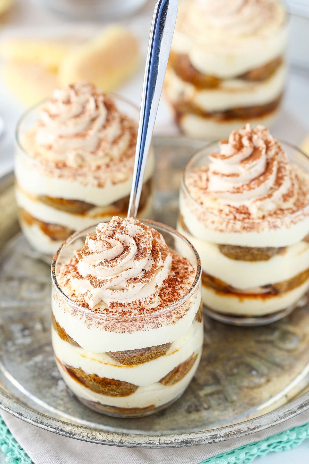 Three tiramisu trifles on a metal plate with a spoon inside one of them