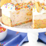 Easy no-bake Funfetti oreo birthday cake cheesecake on a cake stand with a slice taken out of it.