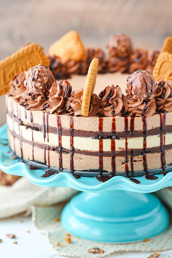 Size view of a whole Icebox Cake on a blue cake stand that is topped with Biscoff cookies, chocolate whipped cream and Ferrero Rocher