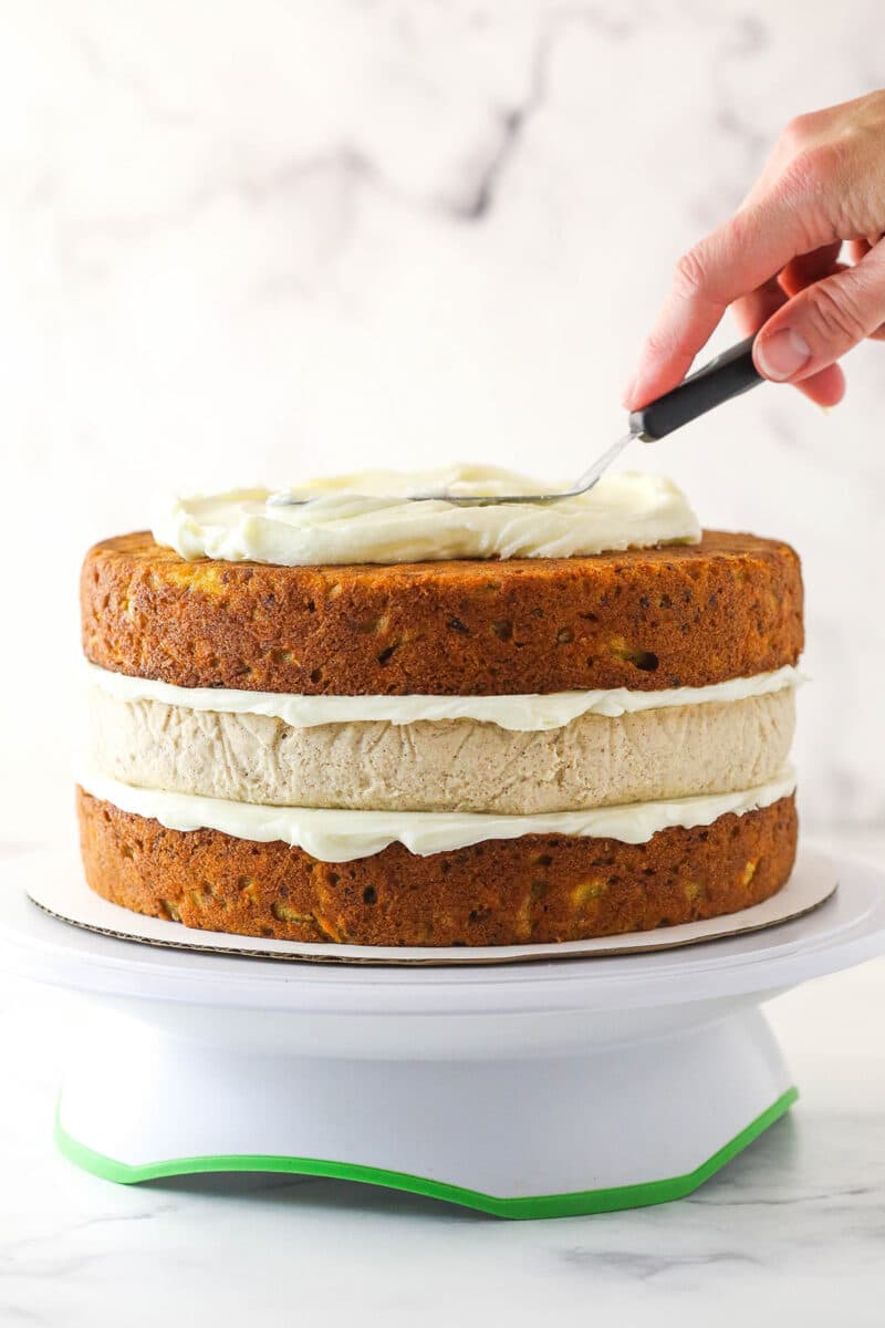 layered cake on turntable with frosting being added on top