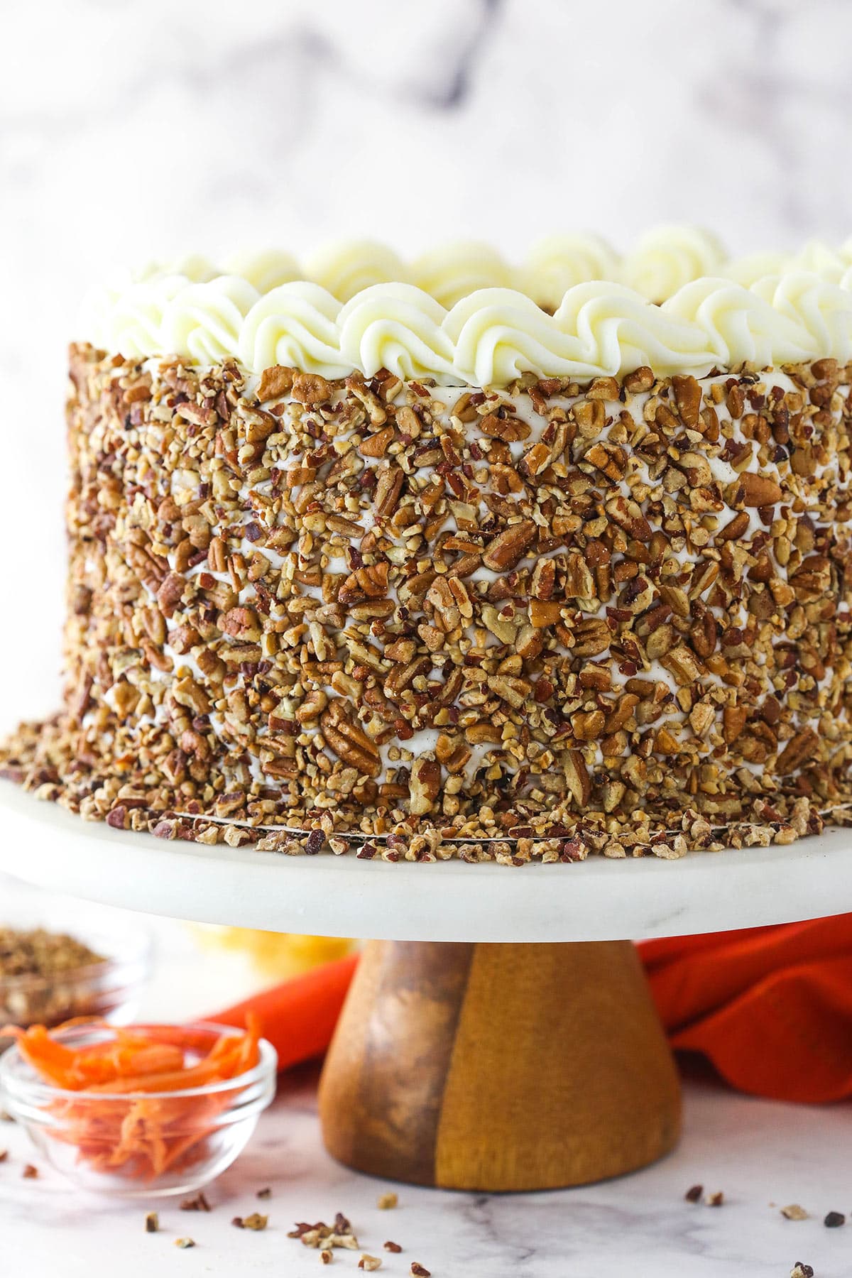 full carrot cake cheesecake cake on cake stand with orange cloth in background
