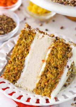 slice of carrot cake cheesecake cake on white plate with pecans, pineapple and carrots in bowls in the background