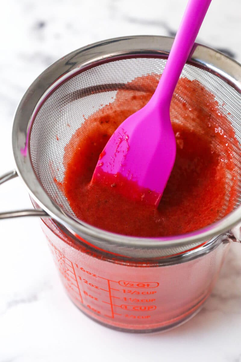 Strawberry sauce is swirled on top of moist, cakey brownies, adding a pop of color and fresh fruit flavor in these strawberry brownies. Strawberry sauce in a strainer over a measuring cup