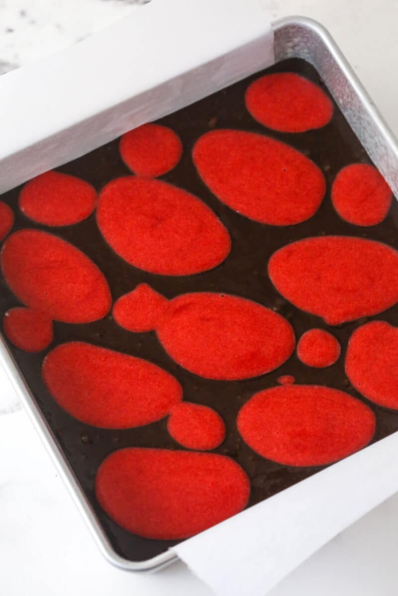 Strawberry sauce is swirled on top of moist, cakey brownies, adding a pop of color and fresh fruit flavor in these strawberry brownies. Dollops of strawberry sauce on top of brownie batter in a square pan
