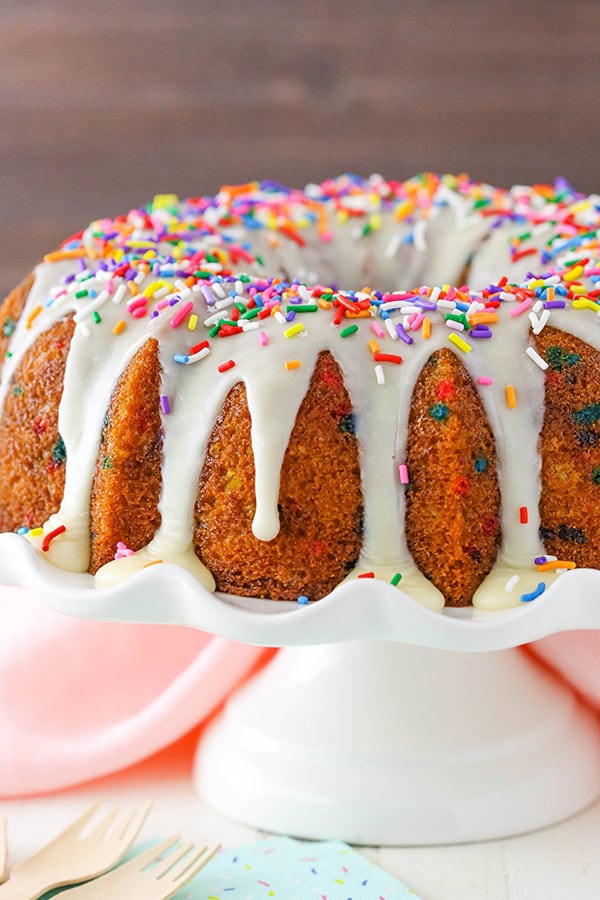 A whole Funfetti Bundt Cake topped with icing and sprinkles on a cake stand