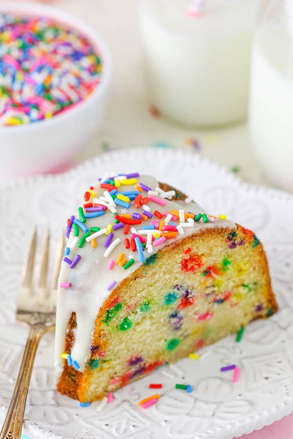 Close up of a slice of Funfetti Cake topped with sprinkles and white icing on white plate