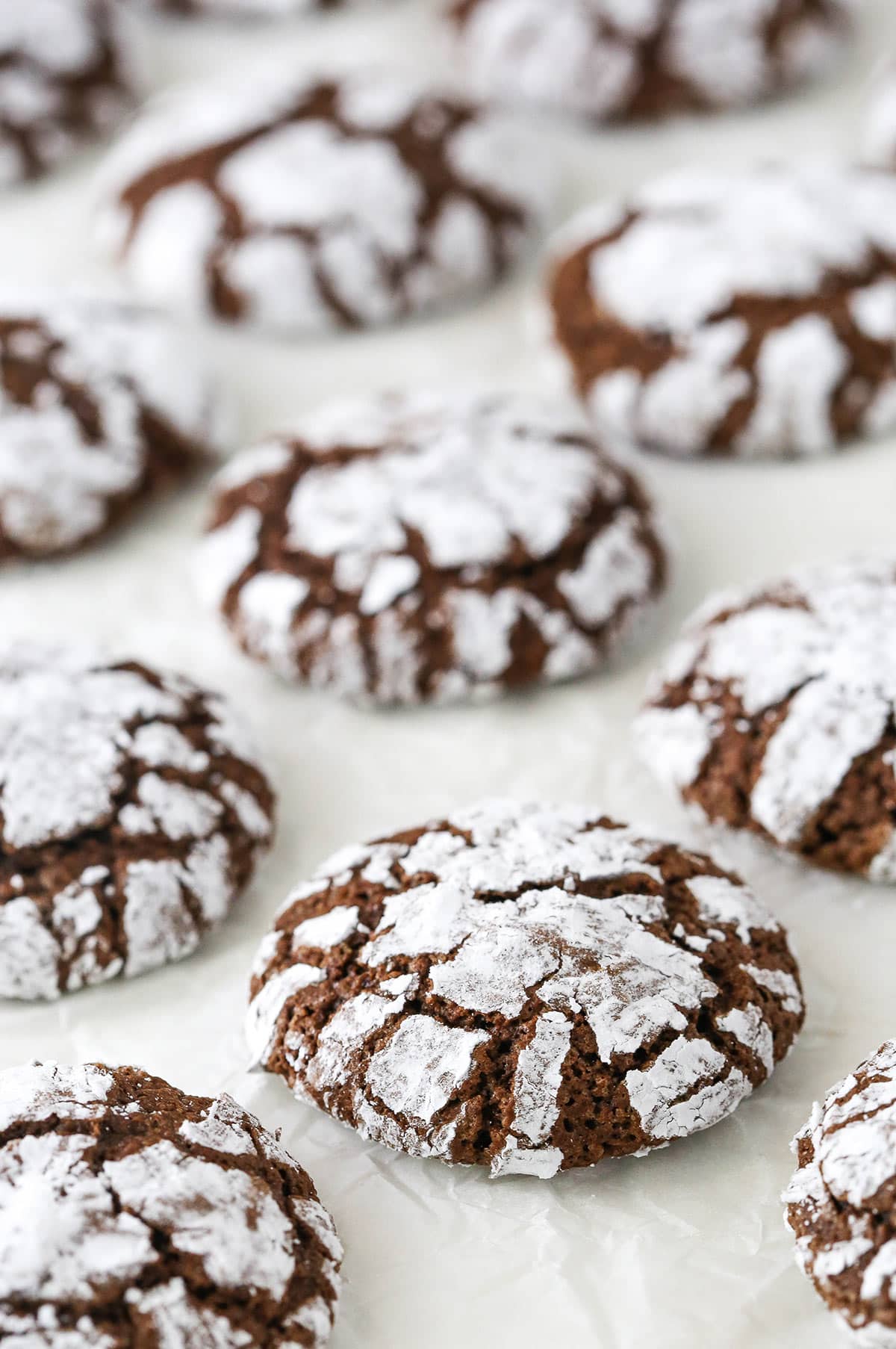 My fudgy chocolate crinkle cookies are ready in 30 minutes! Chocolatey and dusted with powdered sugar, they're the perfect holiday cookies! Chocolate crinkle cookies on a white surface.