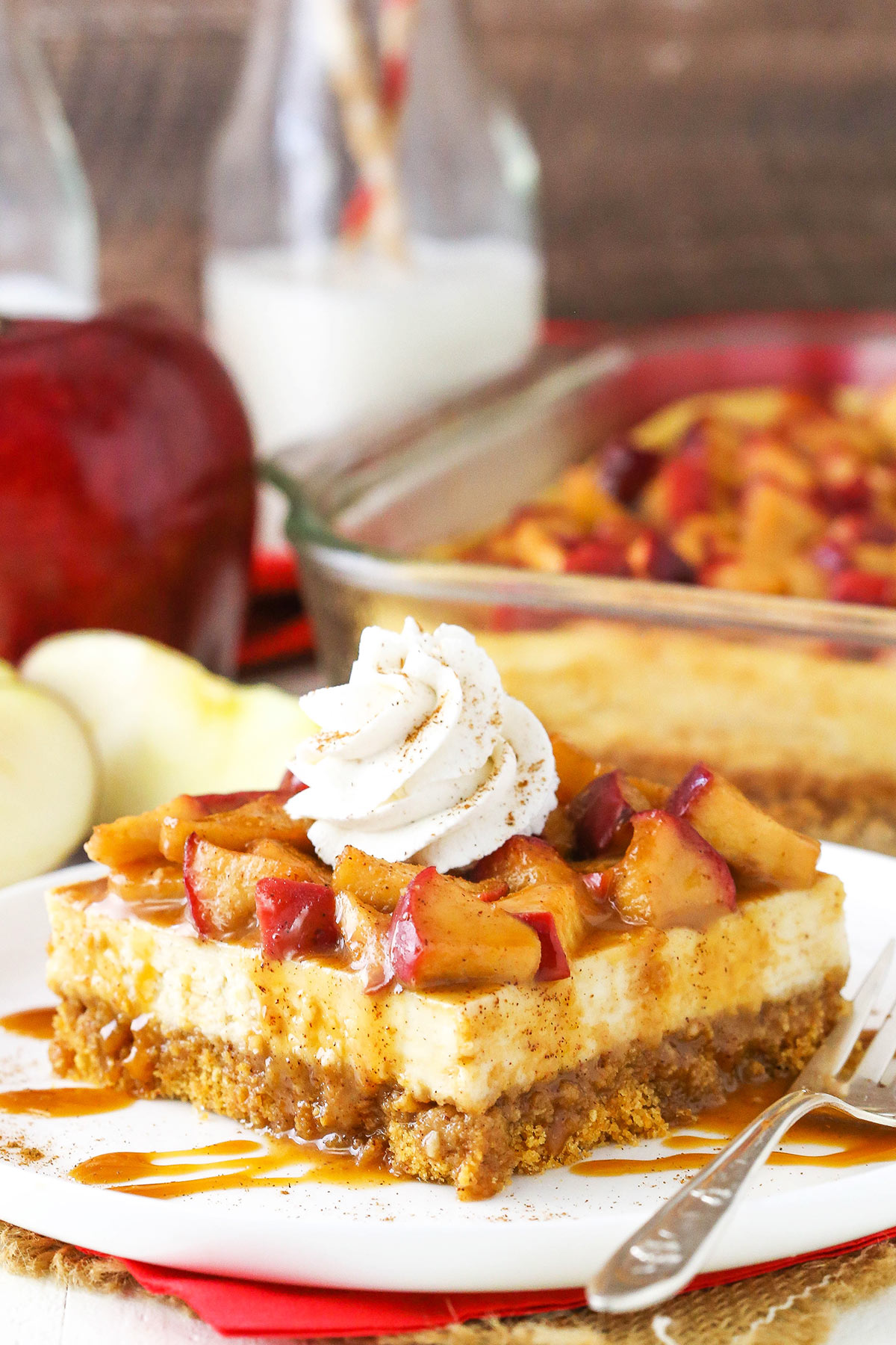 A square of caramel apple cheesecake on a plate with the remaining cheesecake bars in a pan behind it