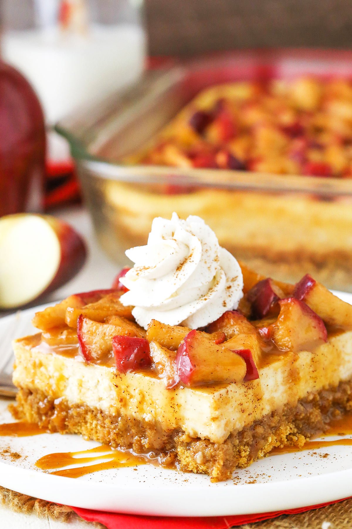 A close-up shot of a piece of caramel apple cheesecake with an apple slice and more cheesecake in the background