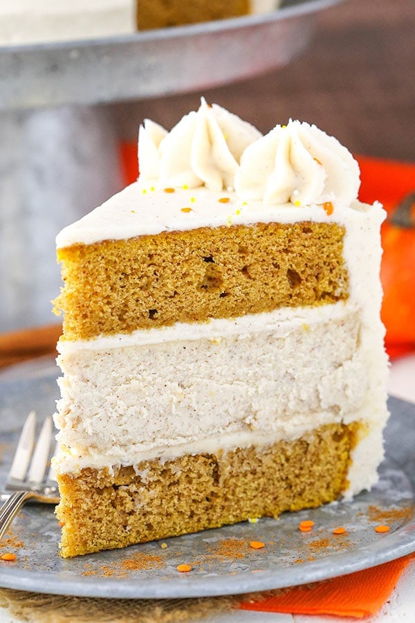 This pumpkin cheesecake cake has two layers of moist pumpkin cake, a layer of spiced cheesecake, and lots of cinnamon cream cheese frosting! Slice of pumpkin cheesecake cake on a plate.