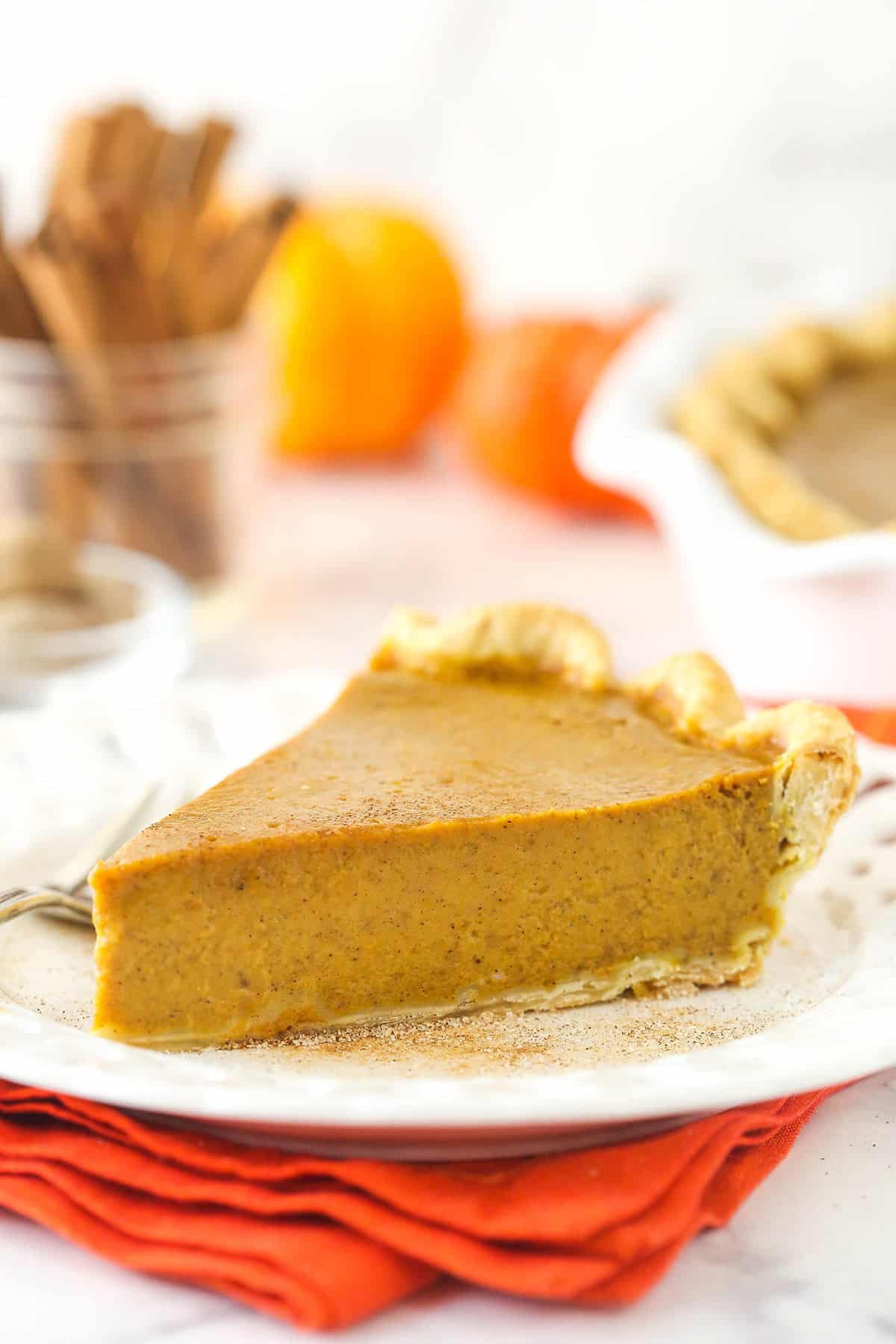 a slice of pumpkin pie on a white plate on an orange napkin