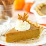 a slice of pumpkin pie on a white plate on an orange napkin with whipped cream and pie crust leaf on top