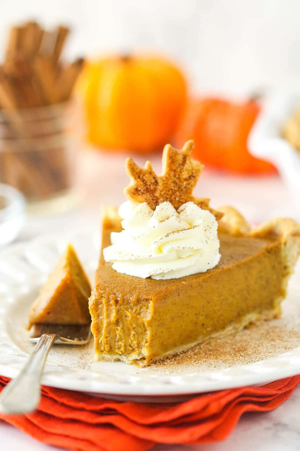 a slice of pumpkin pie with a bite taken on a white plate on an orange napkin