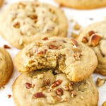 A butter pecan cookie with bite taken out stacked on more cookies.