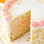 A champagne layer cake on a cardboard cake round with one large slice removed