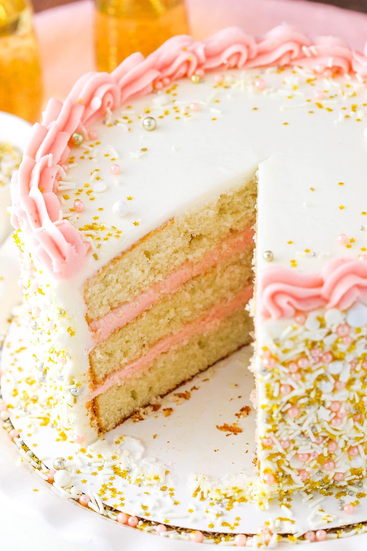 A champagne layer cake on a cardboard cake round with one large slice removed