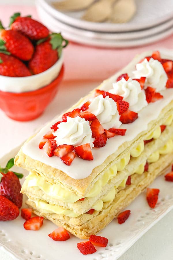 A strawberry napoleon pastry on a platter with homemade whipped cream and fresh strawberry slices on top