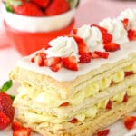 A mille-feuille on a long platter with a bowl containing fresh strawberries in the background