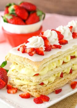 A mille-feuille on a long platter with a bowl containing fresh strawberries in the background