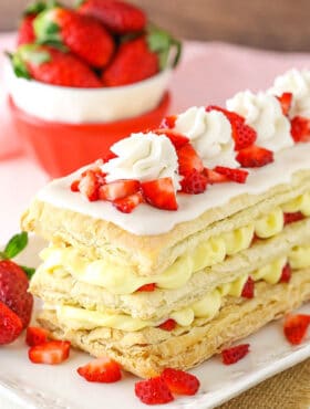 A mille-feuille on a long platter with a bowl containing fresh strawberries in the background