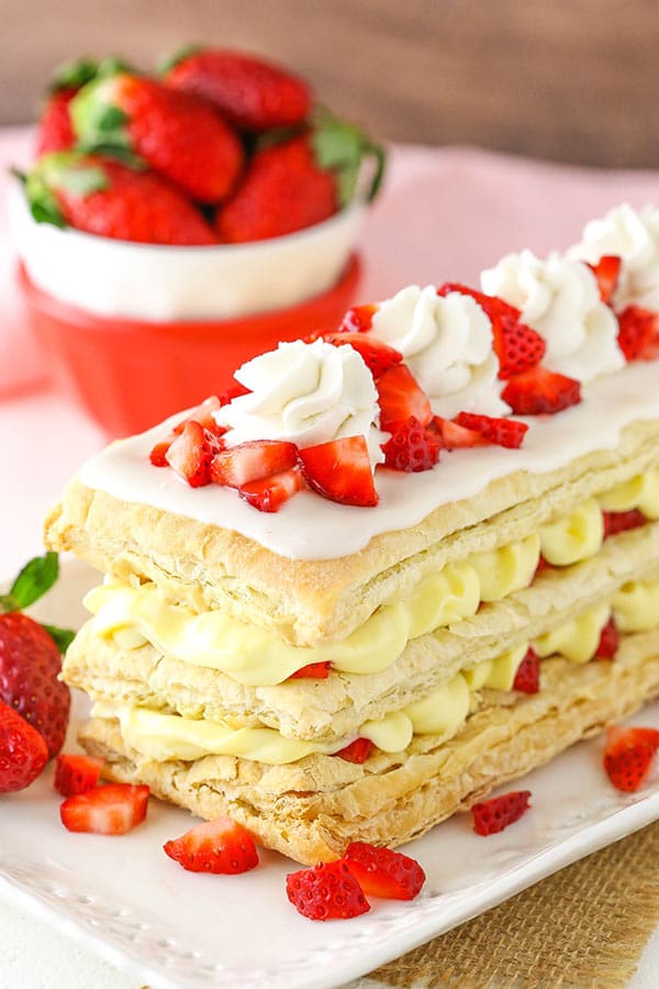 A mille-feuille on a long platter with a bowl containing fresh strawberries in the background