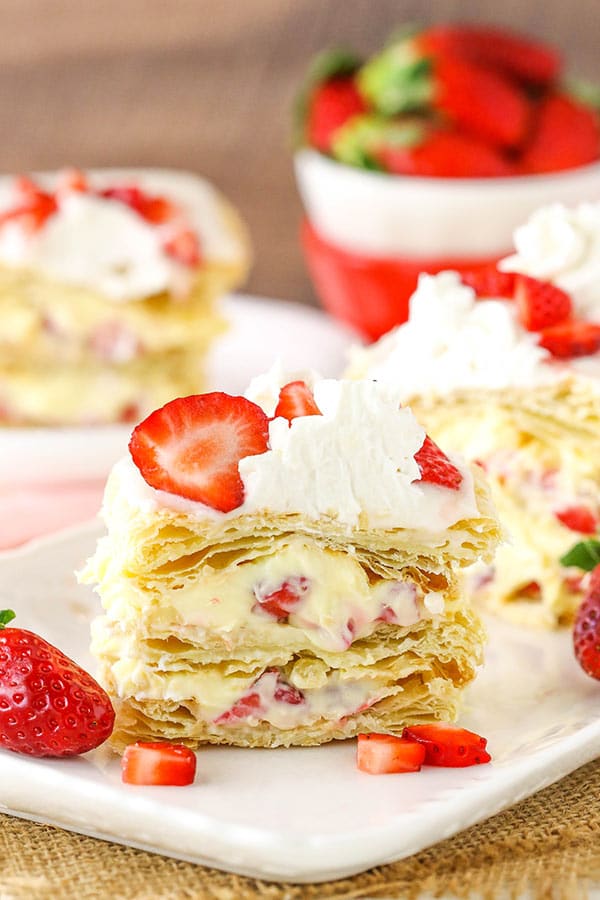 Two strawberry napoleon slices on a serving platter with another helping on a plate in the background