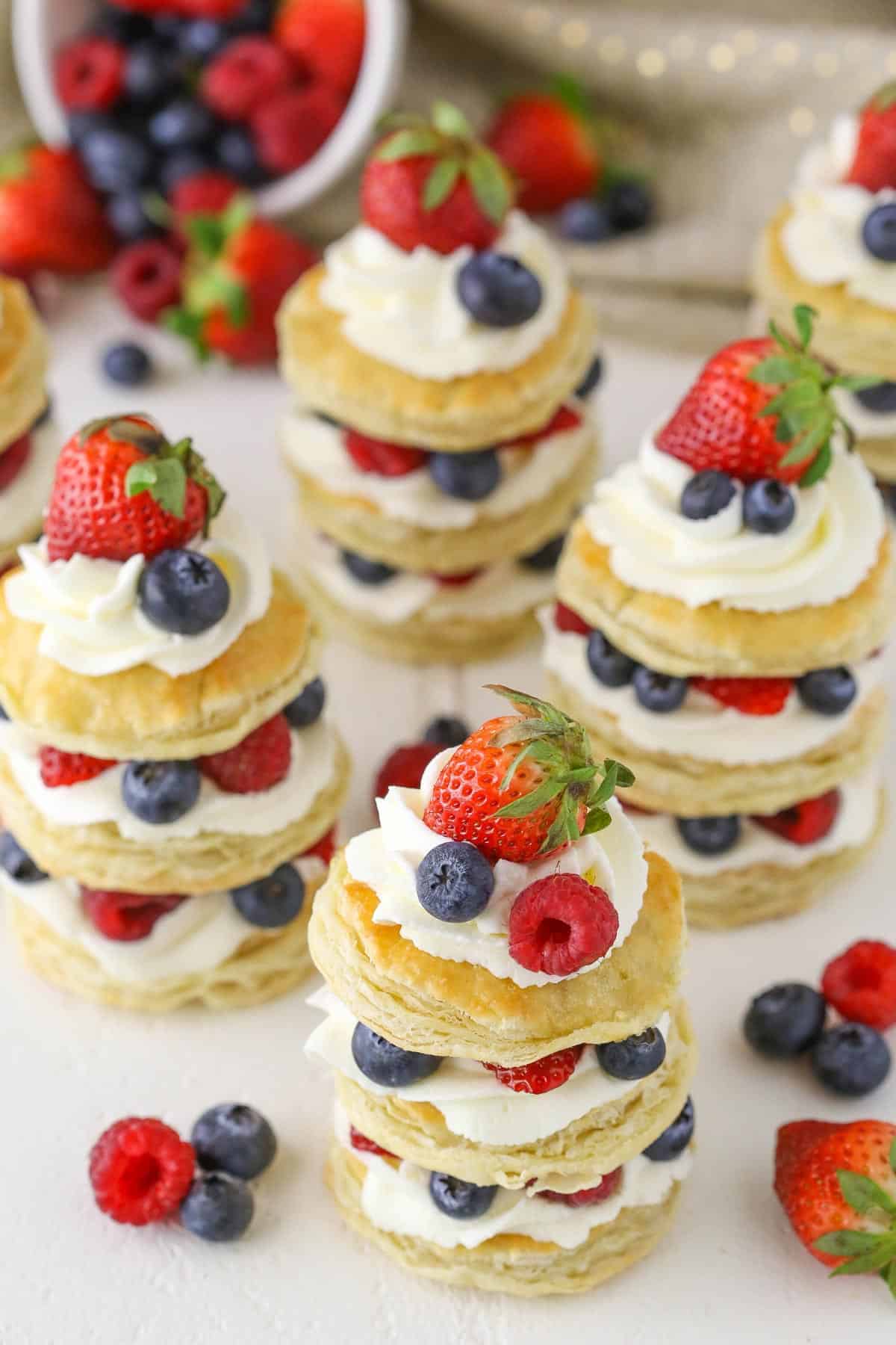Several mini berries and cream mini cakes surrounded by fruit.