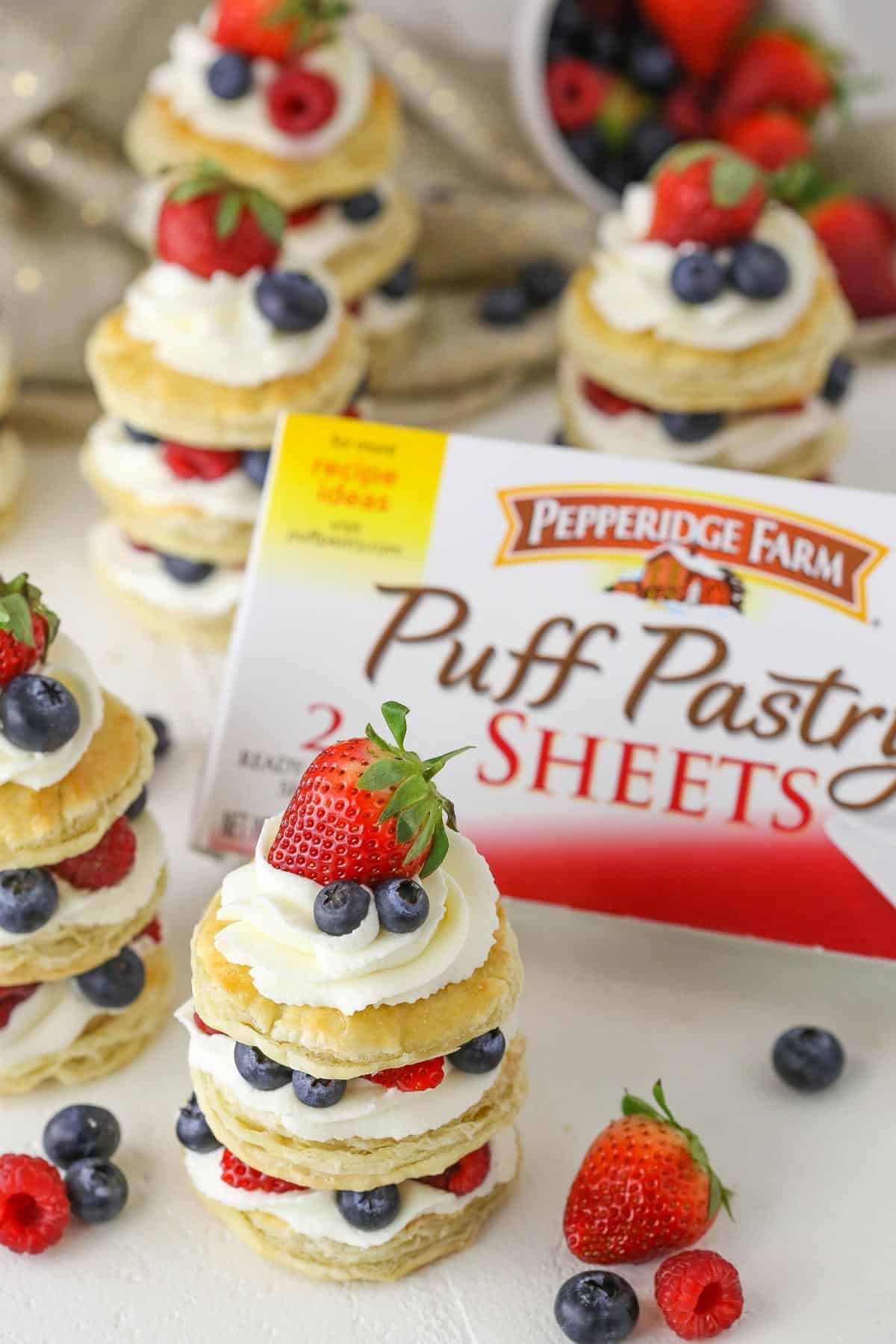 Mini berries and cream puff pastry cakes in front of a box of puff pastry. 