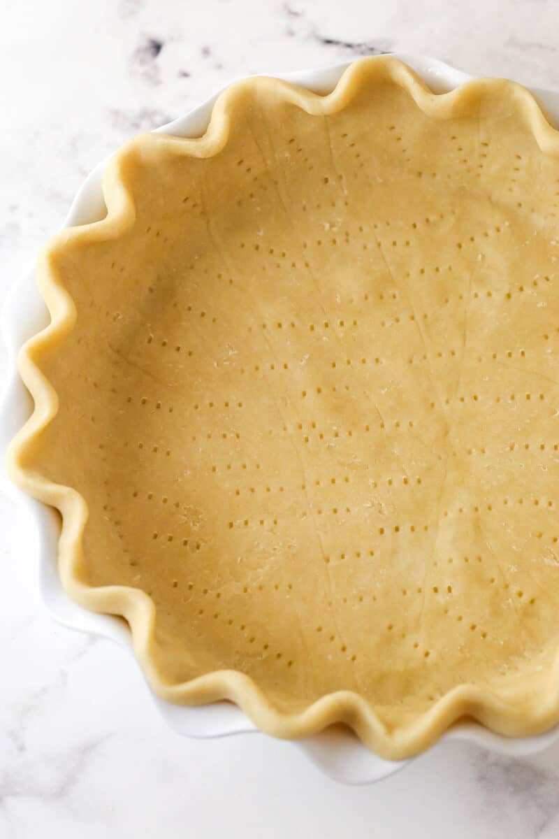 This coconut cream pie is a classic, creamy dessert made from rich coconut custard filling topped with whipped cream in a buttery pie crust. Pie crust inside a pie plate with fork pricks over the bottom.