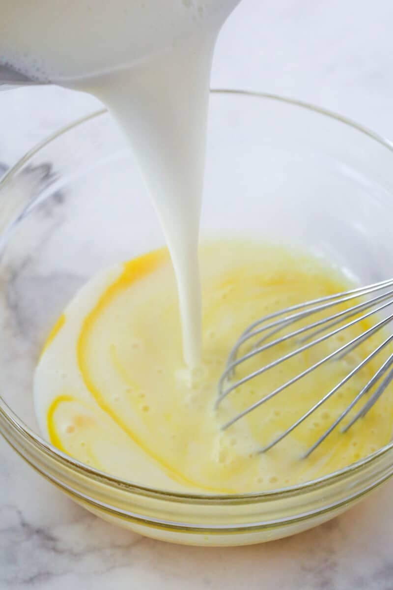 This coconut cream pie is a classic, creamy dessert made from rich coconut custard filling topped with whipped cream in a buttery pie crust. Tempering the eggs in a bowl with the warm milk mixture.