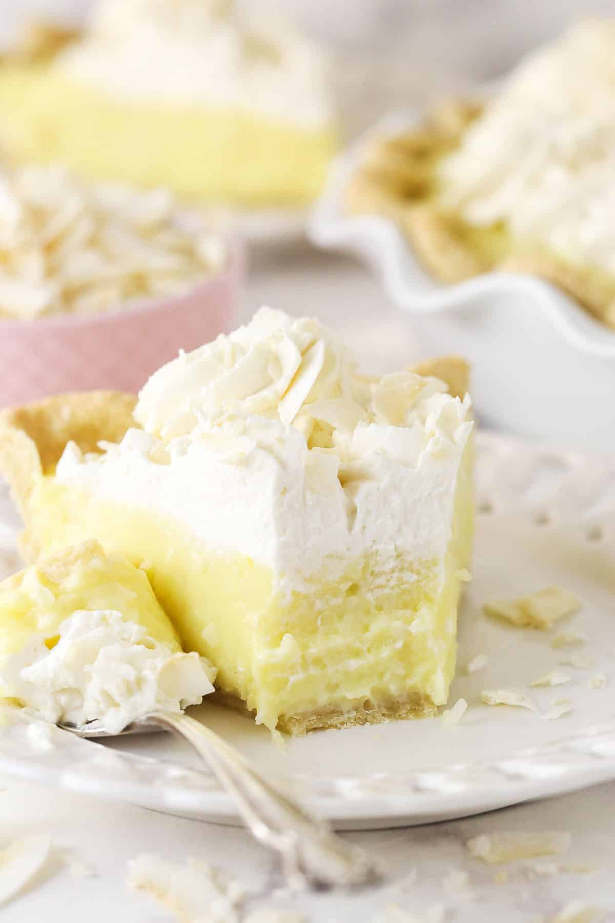 This coconut cream pie is a classic, creamy dessert made from rich coconut custard filling topped with whipped cream in a buttery pie crust. A slice of coconut cream pie on a plate with a forkful taken out of it.