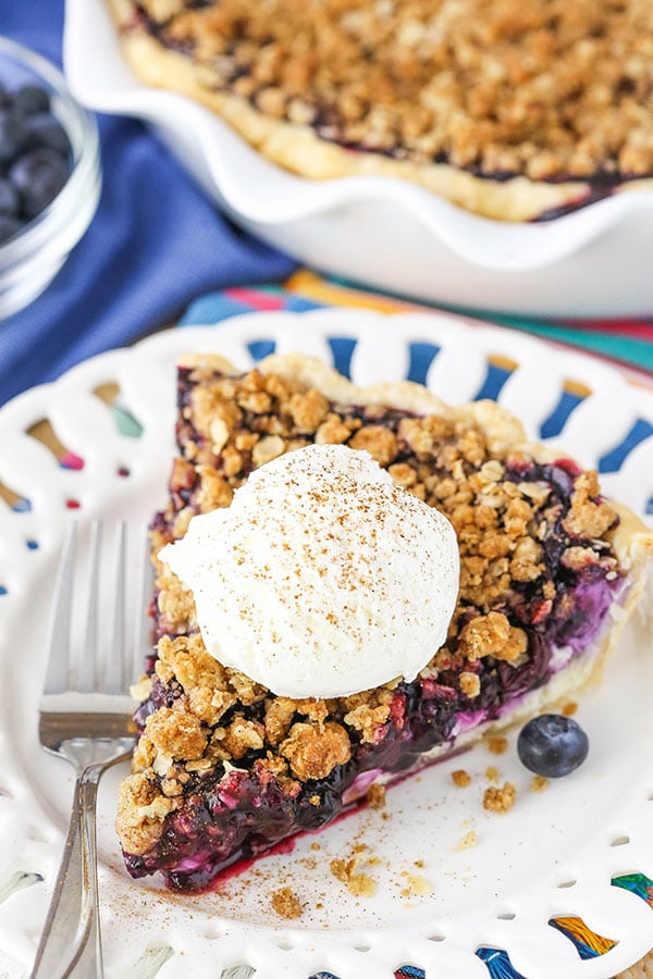 A slice of Blueberry Crumb Cheesecake Pie with ice cream on top on a white plate. 